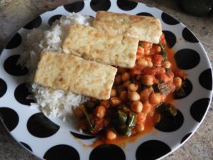 dished up plate of chickpea and spinach curry with tofu slices on top